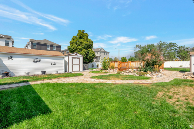 7391 Elm Street Midvale, UT 84047 - Photo 26 of 38 Expansive backyard featuring a manicured lawn, a raised wood deck, paved pathways, and 2 storage sheds with lights and electricity