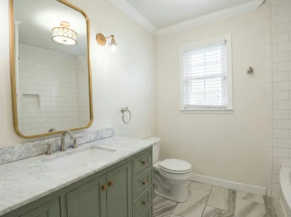 a bathroom with a granite countertop sink toilet a large mirror and a window