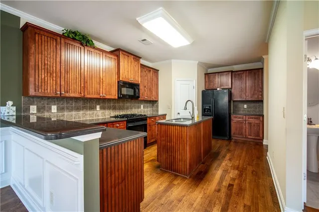 a kitchen with stainless steel appliances granite countertop wooden cabinets a refrigerator a stove a sink and dishwasher with wooden floor