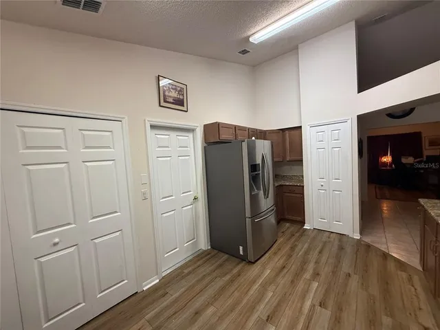 a view of a refrigerator in kitchen and an empty room with wooden floor