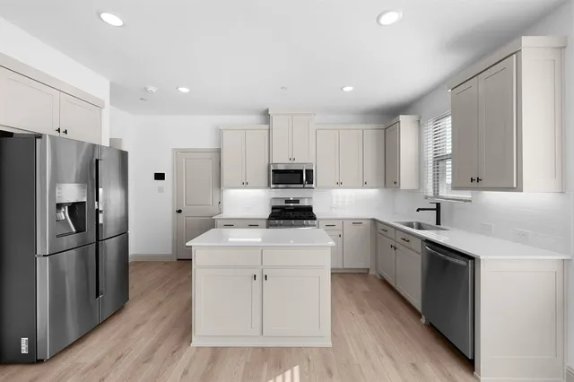 a kitchen with stainless steel appliances granite countertop a stove top oven a refrigerator and white cabinets with wooden floors