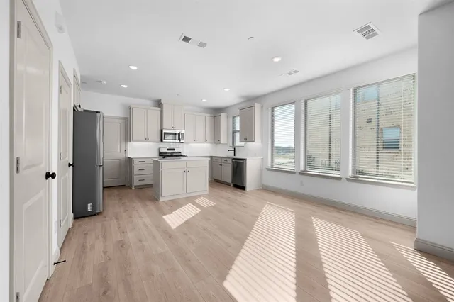 a large white kitchen with stainless steel appliances granite countertop a refrigerator oven a sink dishwasher and white cabinets with wooden floor