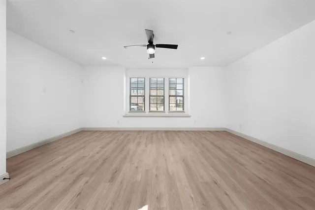 an empty room with wooden floor ceiling fan and windows