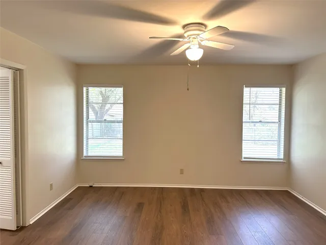 an empty room with wooden floor chandelier fan and windows