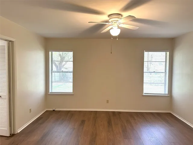an empty room with wooden floor chandelier fan and windows
