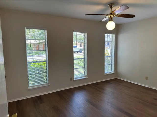 a view of an empty room with wooden floor and fan
