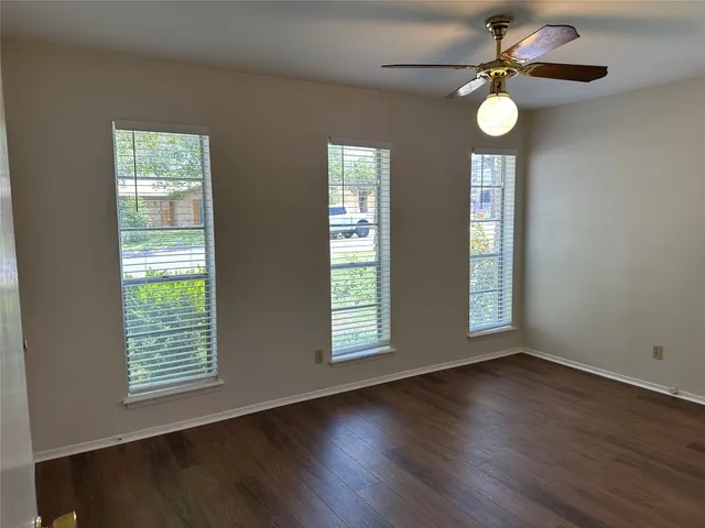 a view of an empty room with wooden floor and fan