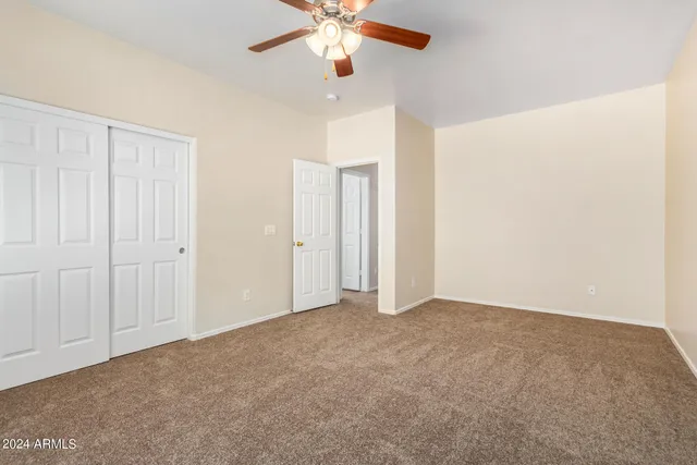 an empty room with chandelier fan and windows