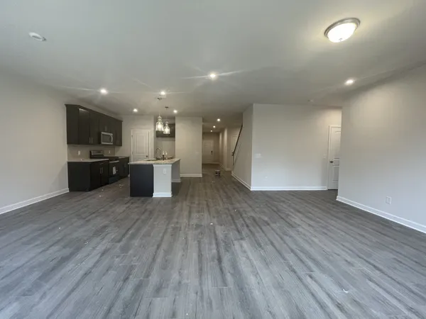 an empty room with wooden floor and kitchen view
