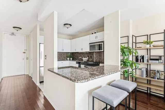 a kitchen with stainless steel appliances granite countertop a refrigerator a stove a sink dishwasher and white cabinets with wooden floor