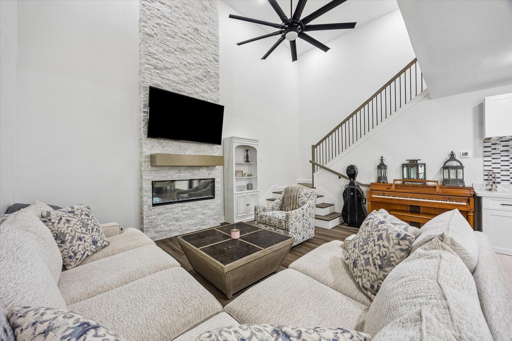 1420 Indiana Street Houston, TX 77006 - Photo 10 of 31 This living room features a high ceiling with a large fan, a modern stone fireplace. The room includes a staircase with sleek railings, creating a warm and inviting atmosphere.