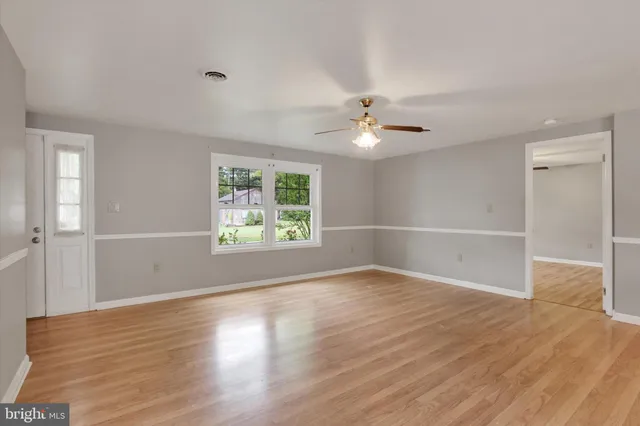 an empty room with wooden floor fan and windows