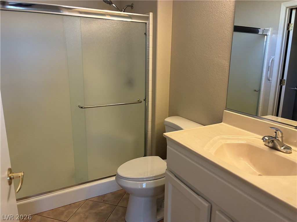 Functional bathroom featuring a shower with sliding doors, a well-lit vanity, and tiled flooring.