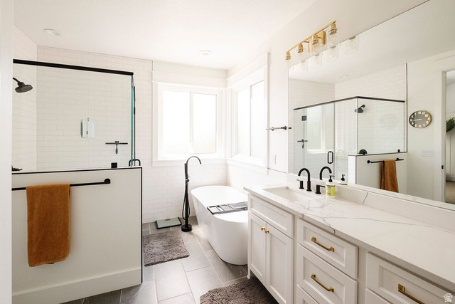 924 Country Lane Farmington, UT 84025 - Photo 26 of 91 Modern bath featuring a freestanding soaking tub, a separate glass-enclosed shower with subway tile, a dual-sink vanity with quartz countertops, and gold-finish hardware