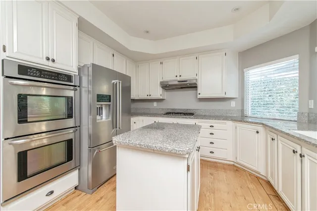 a kitchen with granite countertop white cabinets appliances and a window