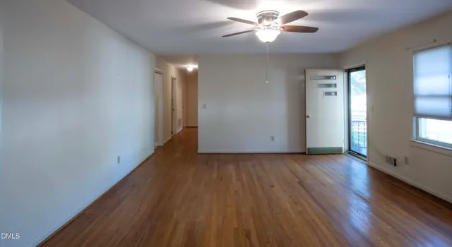 an empty room with wooden floor chandelier fan and windows