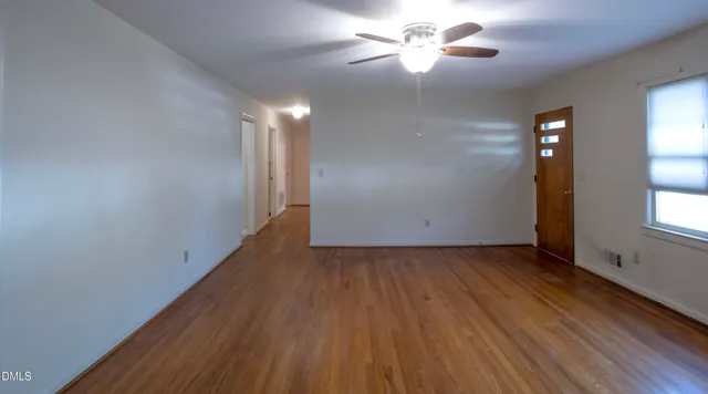 an empty room with wooden floor chandelier fan and windows