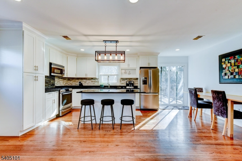 6 Elm Avenue Warren, NJ 07059 - Photo 7 of 29 a kitchen with stainless steel appliances granite countertop a stove top oven a refrigerator a dining table and chairs with wooden floor