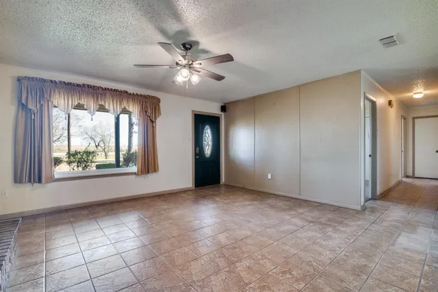 a view of an empty room with window and chandelier fan