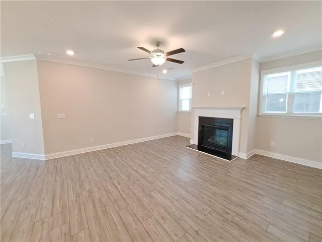 an empty room with wooden floor a ceiling fan a fireplace and windows