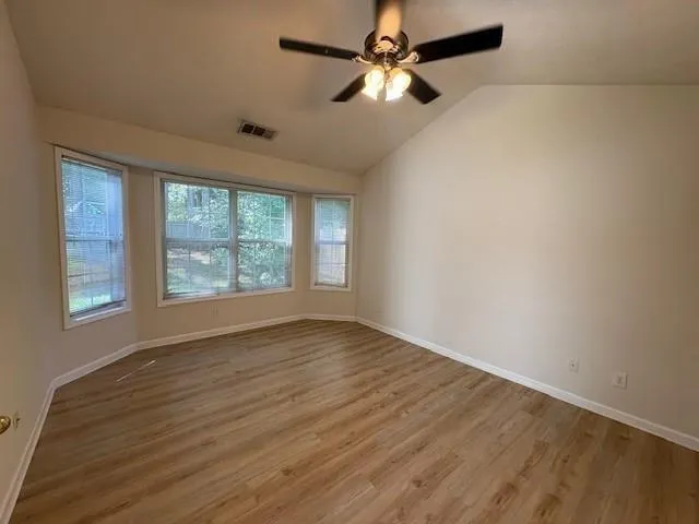 an empty room with wooden floor chandelier fan and windows
