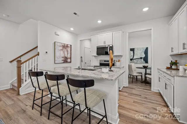 a kitchen with stainless steel appliances granite countertop a stove top oven a sink a refrigerator and white cabinets with wooden floor