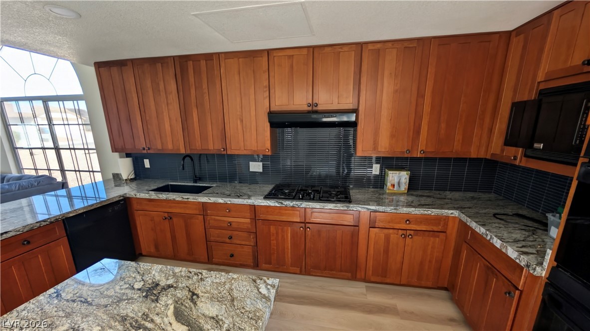 104 Appian Way Henderson, NV 89002 - Photo 26 of 37 Kitchen featuring wood finish cabinetry, light stone counters, black appliances, light wood-style flooring, and backsplash