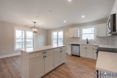 a large white kitchen with granite countertop a stove top oven a sink a dishwasher and wooden cabinets with wooden floor