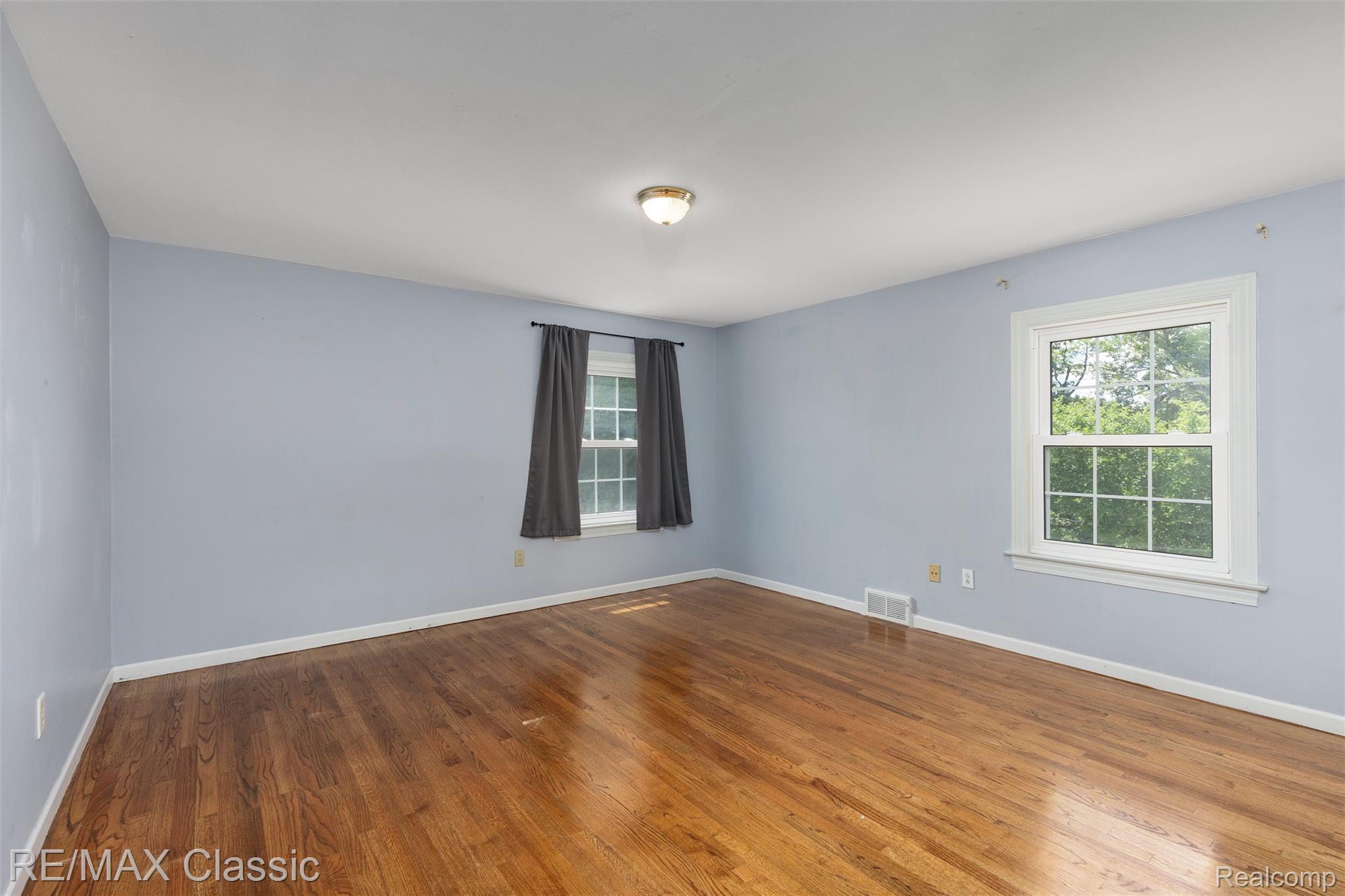 4268 Covered Bridge Road Bloomfield Hills, MI 48302 - Photo 16 of 35 Spacious room featuring wood-finish flooring, two large windows, white trim, and a ceiling-mounted light fixture