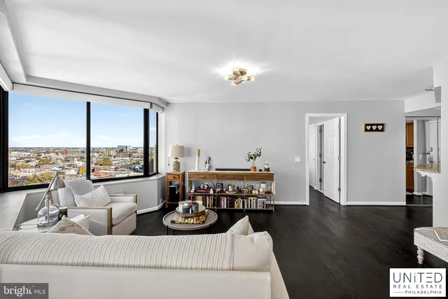 a living room with furniture two large window and wooden floor