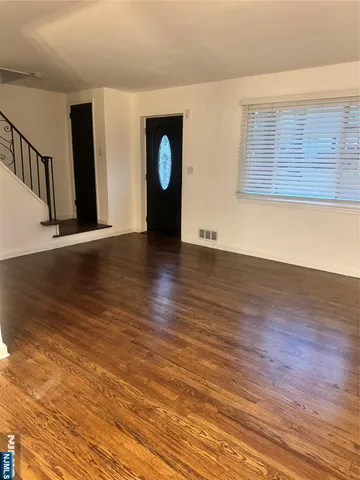a view of an empty room with wooden floor and fan