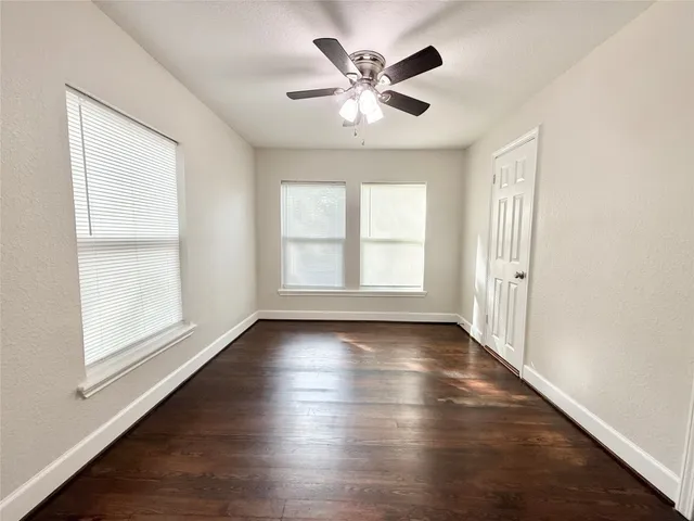 an empty room with wooden floor chandelier fan and windows