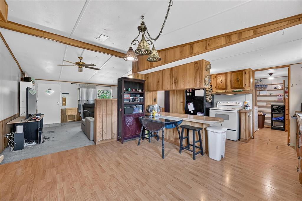 736 Little Joe Road Sanger, TX 76266 - Photo 15 of 17 Open-concept main living area featuring wood-finish flooring, a kitchen with light wood cabinetry, a breakfast bar with seating, a ceiling fan, and a built-in shelving unit