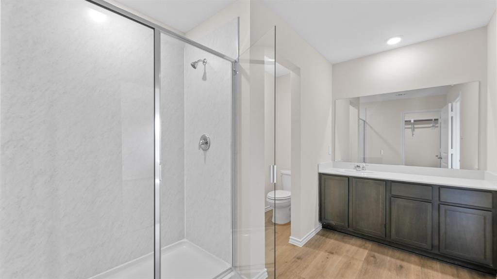 657 Glee Stem Road Lavon, TX 75166 - Photo 17 of 26 Spacious bathroom featuring a glass-enclosed shower, a wide vanity with ample storage, a large wall-mounted mirror, wood-finish flooring, and recessed ceiling lighting