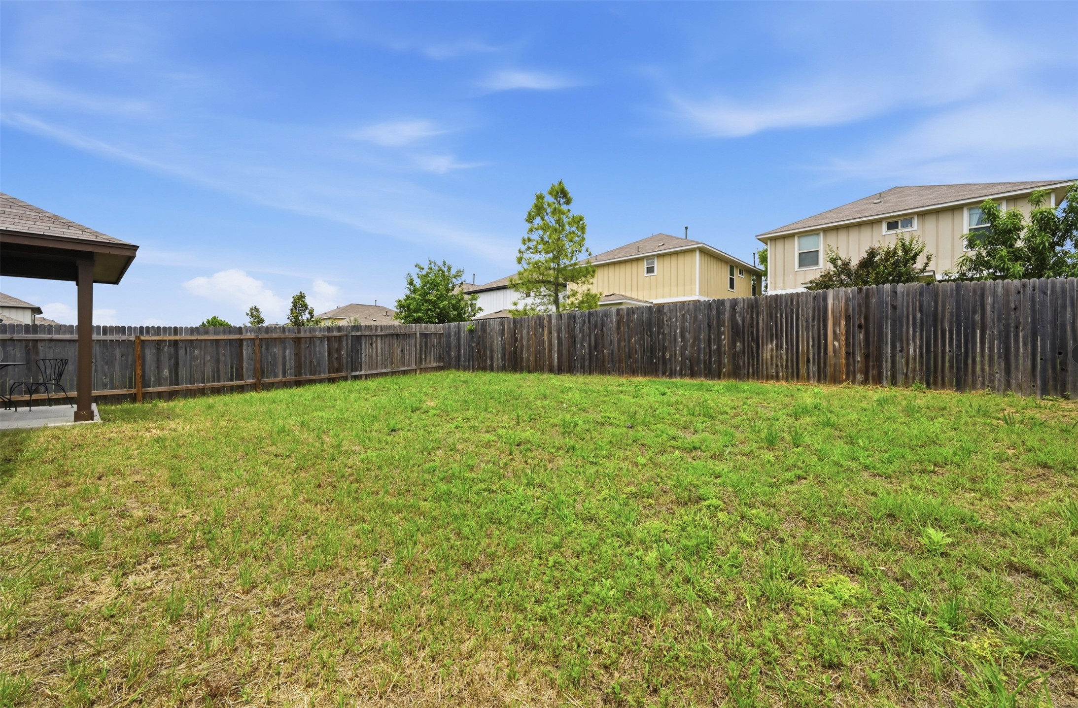 303 Limerick Road Buda, TX 78610 - Photo 20 of 23 Expansive backyard featuring a large grass lawn, full perimeter wood privacy fencing, and a covered patio area with a concrete surface