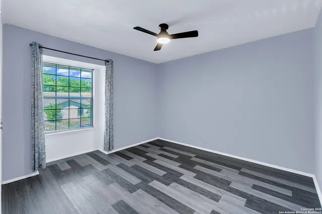 an empty room with wooden floor chandelier fan and windows