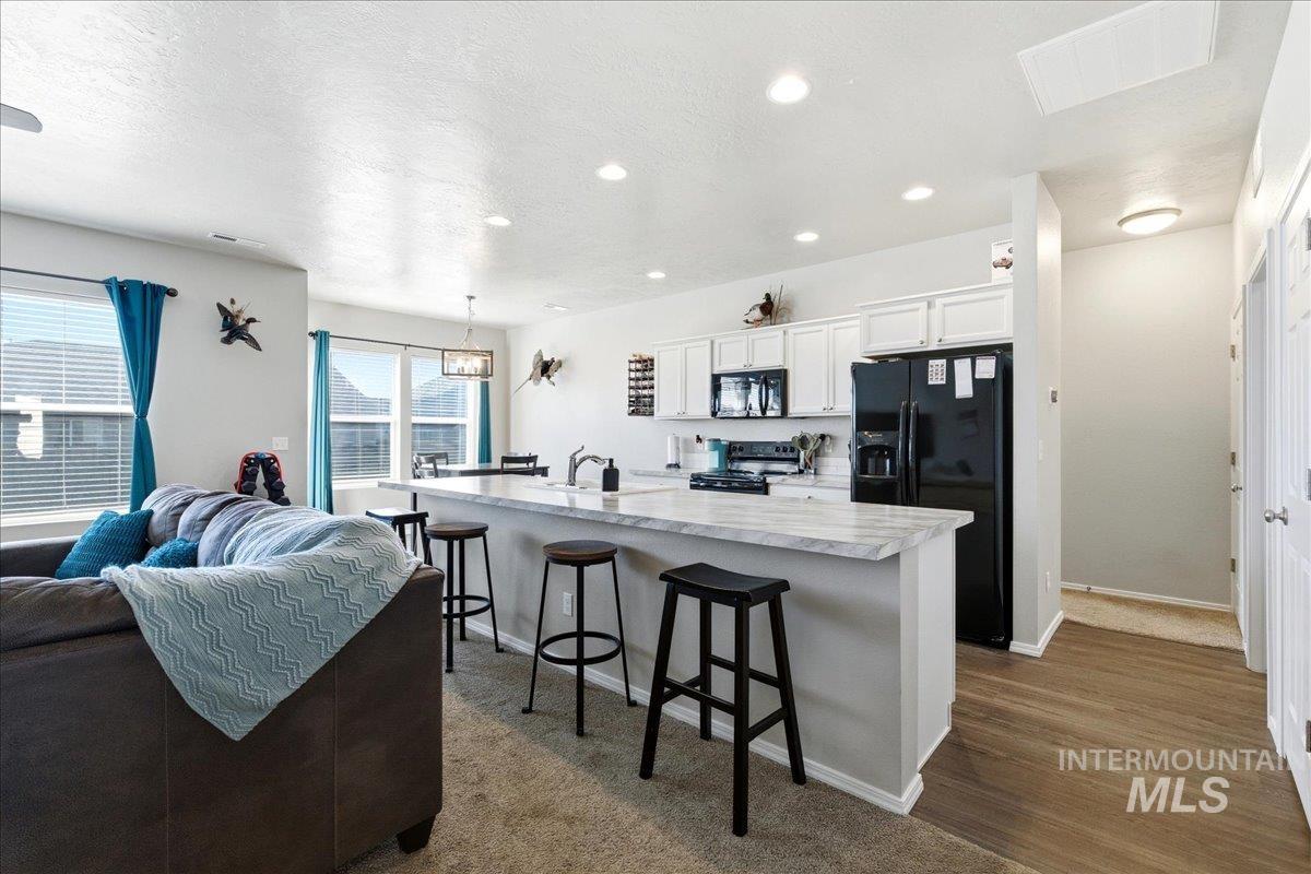 Kitchen featuring a kitchen bar, light countertops, white cabinetry, black appliances, and an island with sink