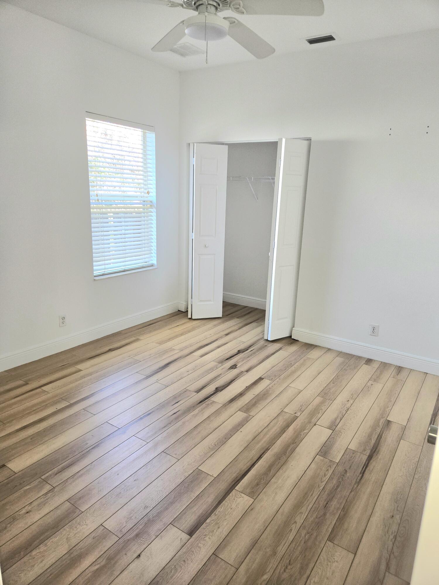 2472 Southwest Valnera Street Port St. Lucie, FL 34953 - Photo 23 of 30 an empty room with wooden floor chandelier fan and windows
