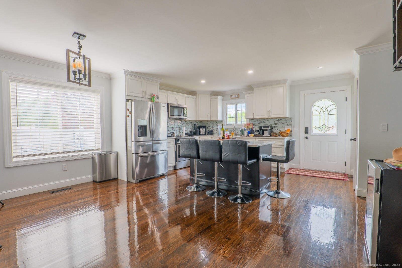 a open dining room with stainless steel appliances kitchen island granite countertop a refrigerator a stove a dining table and chairs with wooden floor