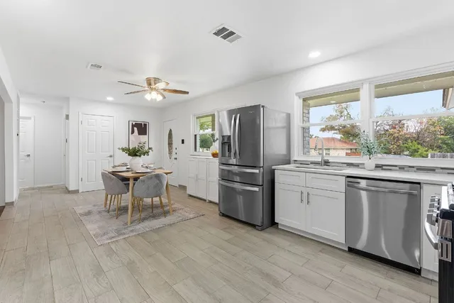 a open kitchen with stainless steel appliances granite countertop a stove top oven a sink dishwasher a dining table and chairs with wooden floor