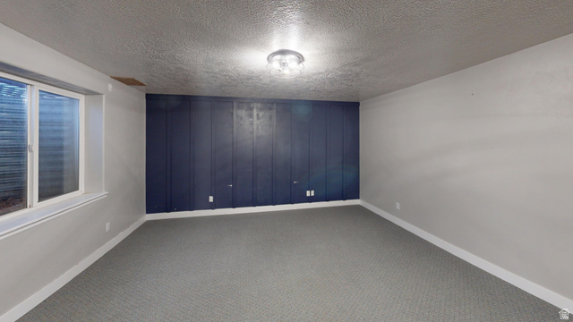 9029 North Treasureton Road Preston, ID 83263 - Photo 17 of 31 Carpeted spare room featuring a textured ceiling, wooden walls, and an accent wall
