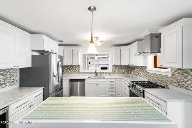 a kitchen with stainless steel appliances kitchen island granite countertop a refrigerator a sink dishwasher a stove with white cabinets and wooden floor