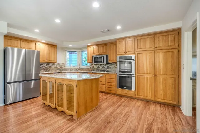 a kitchen with stainless steel appliances granite countertop a refrigerator a stove and a sink with wooden floor
