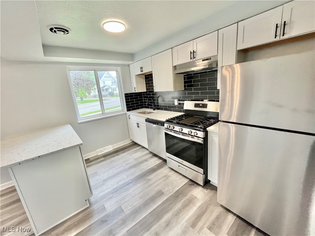 2868 Noble Road, Unit 16 Cleveland, OH 44121 - Photo 4 of 6 Kitchen with appliances with stainless steel finishes, white cabinets, backsplash, under cabinet range hood, and light stone counters