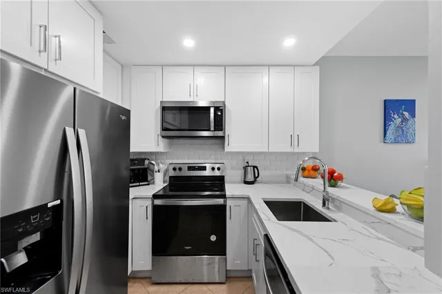 a kitchen with stainless steel appliances a stove a sink a refrigerator white cabinets and wooden floor