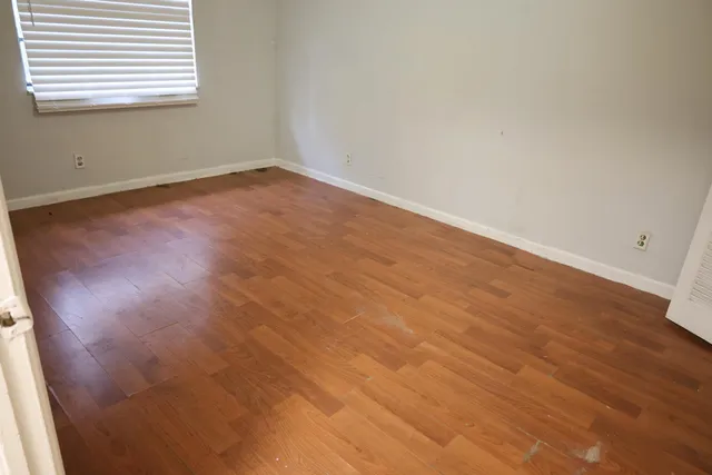 a view of an empty room with wooden floor and a window