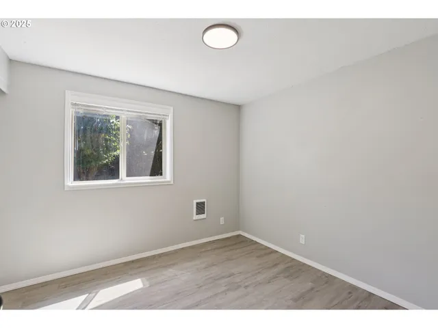 a view of an empty room with wooden floor and fan