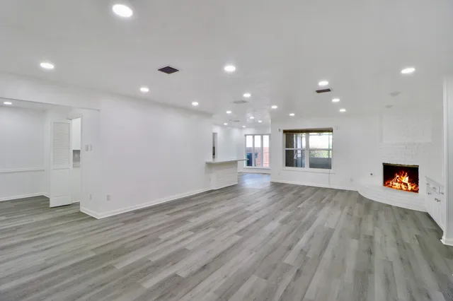 a view of an empty room and a kitchen with wooden floor