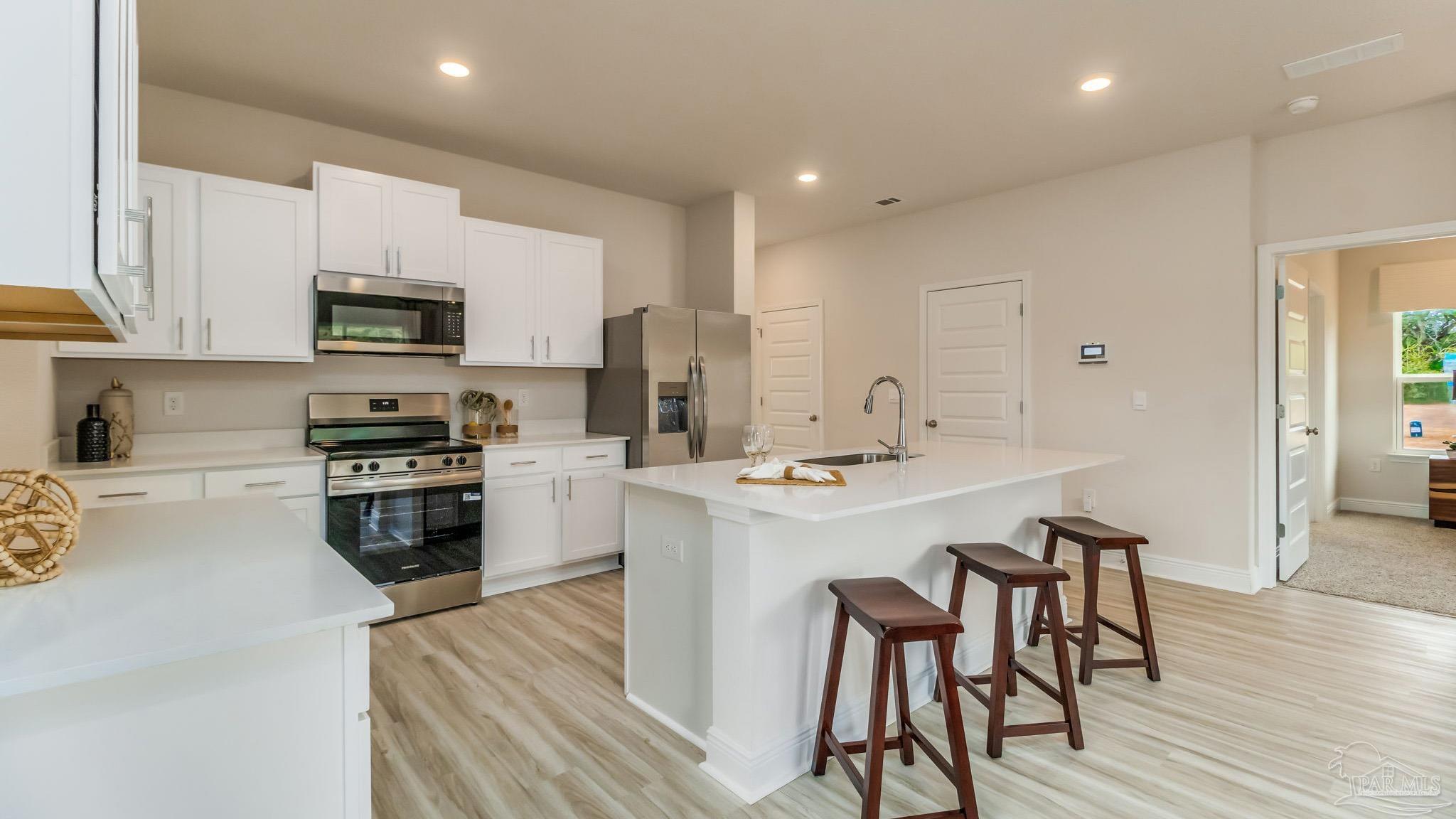 8685 Bluebell Street Milton, FL 32583 - Photo 6 of 30 a kitchen with stainless steel appliances a stove a sink a microwave a refrigerator and white cabinets with wooden floor