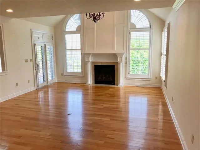 an empty room with wooden floor fireplace and windows